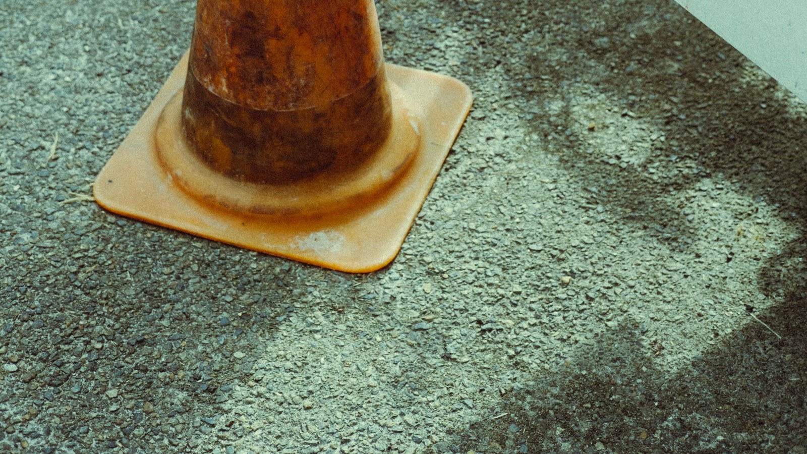 Close-up of a weathered orange traffic cone base resting on coarse asphalt under bright daylight.