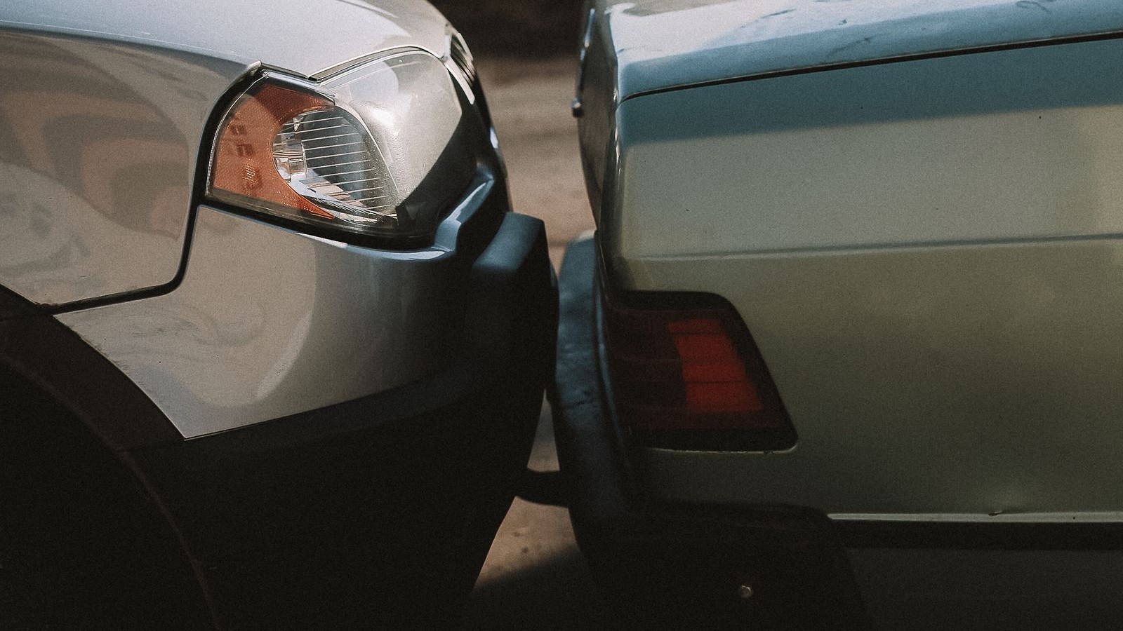 Close-up of the front of a silver vehicle touching the rear bumper of a light green sedan after a minor collision, with no people or logos visible.