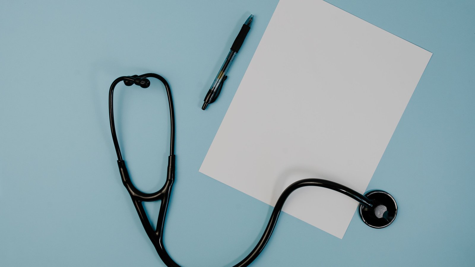 Black stethoscope and a pen resting on a blank sheet of white paper against a light blue background.