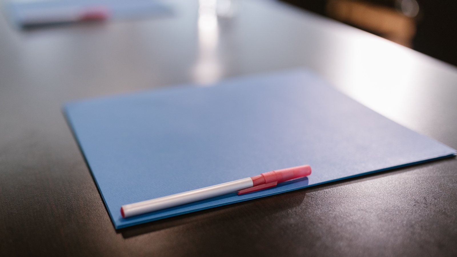 Blank blue paper folder with a pen resting on it on a dark conference table.